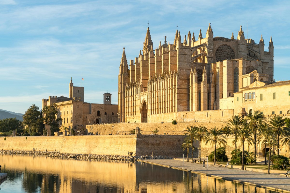 Gothic cathedral in Palma de Mallorca, reflecting in water with clear sky.