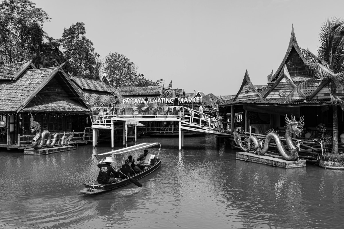 Black and white view of Pattaya's traditional floating market with a boat and Thai architecture.