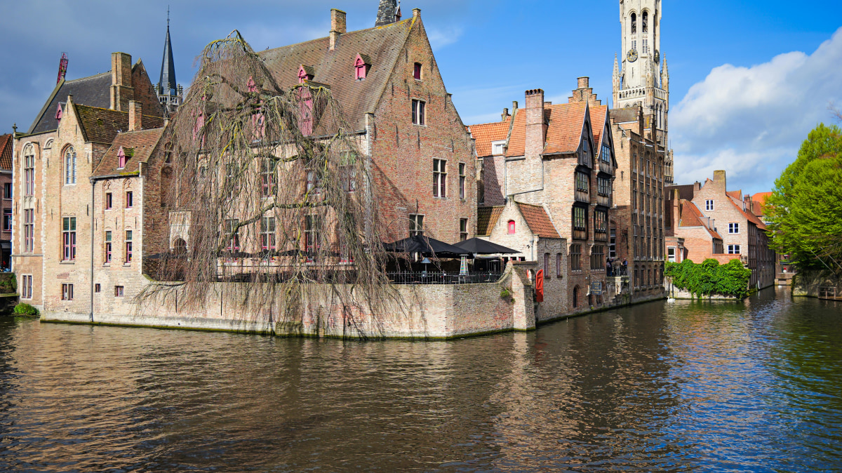 Scenic view of Bruges with historic buildings and canal, featuring the iconic Belfry Tower.