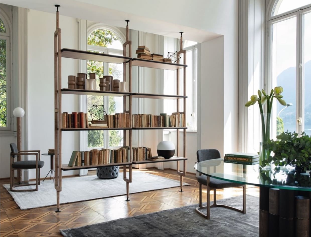 Living room with high ceiling, table with glass top, open bookcase filled with books.