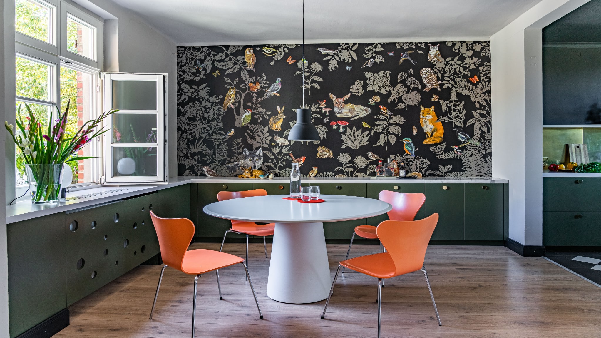 Dining room, vegetal and animal print wallpaper, white table and orange resin chairs.