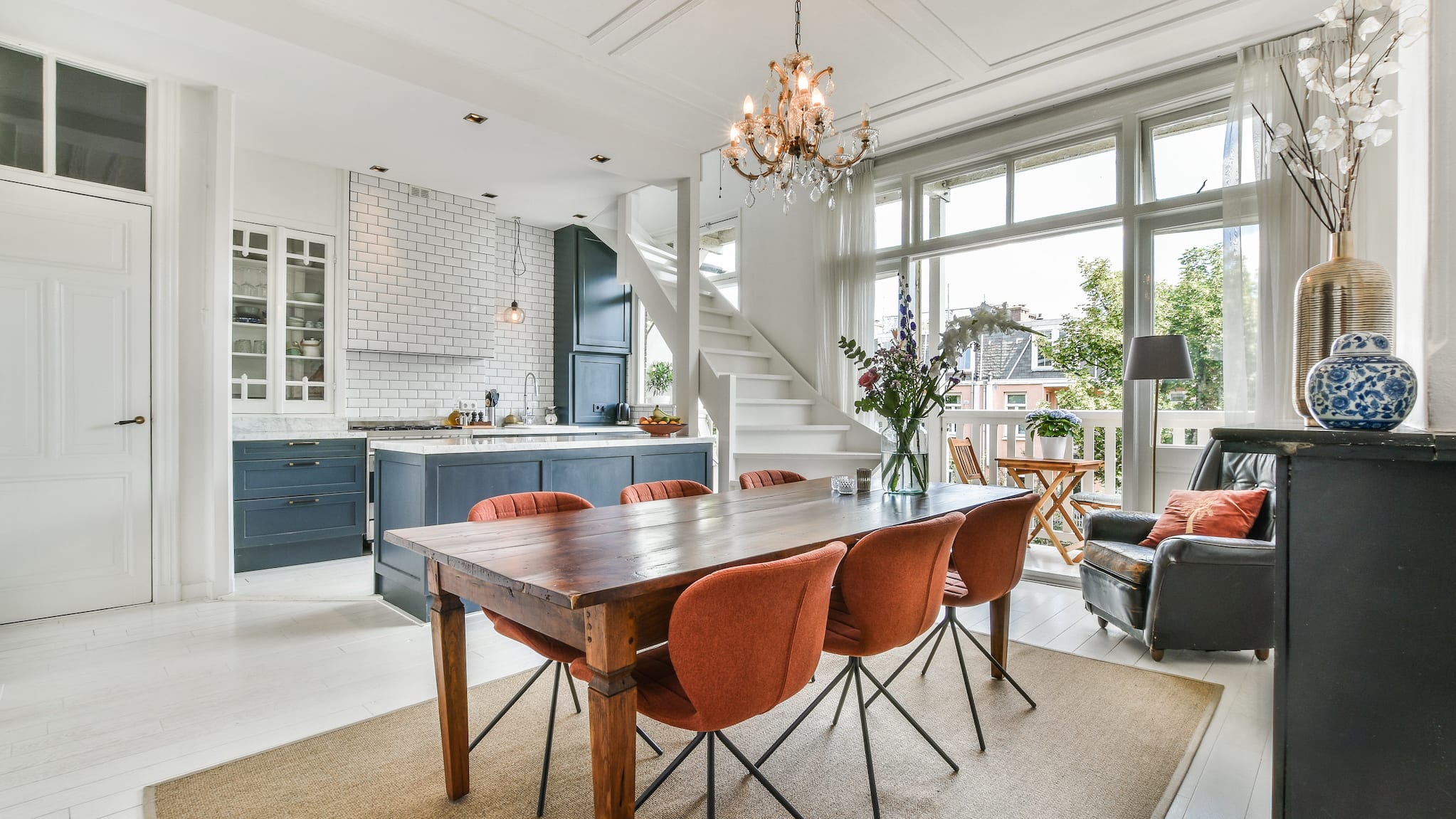 Open concept kitchen and dining room. White brick wall, vintage wood table and orange fabric chairs.