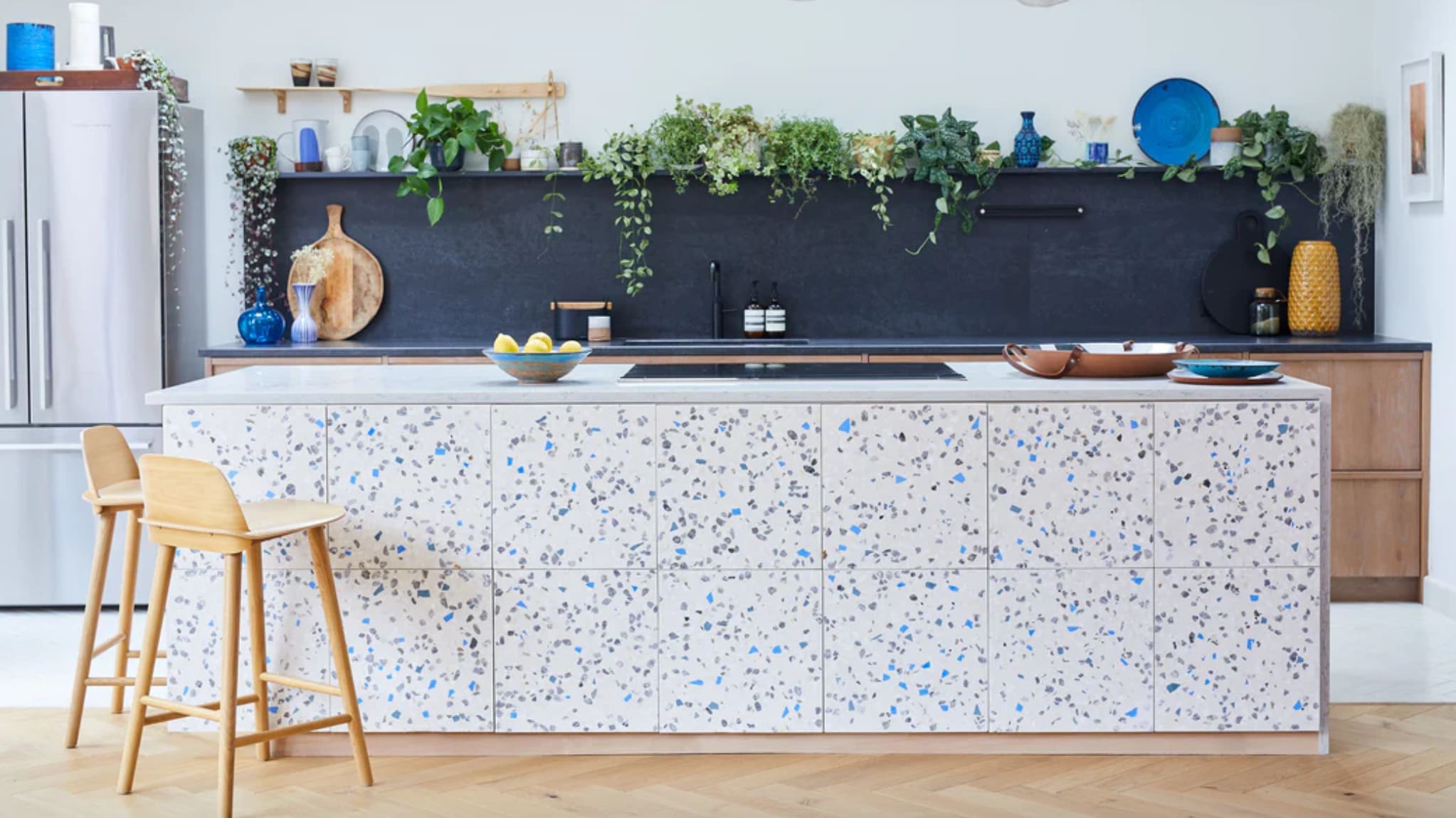 Cuisine bleu et blanc, îlot à motif de terrazzo, tabourets de bois, dosseret marine, plantes vertes