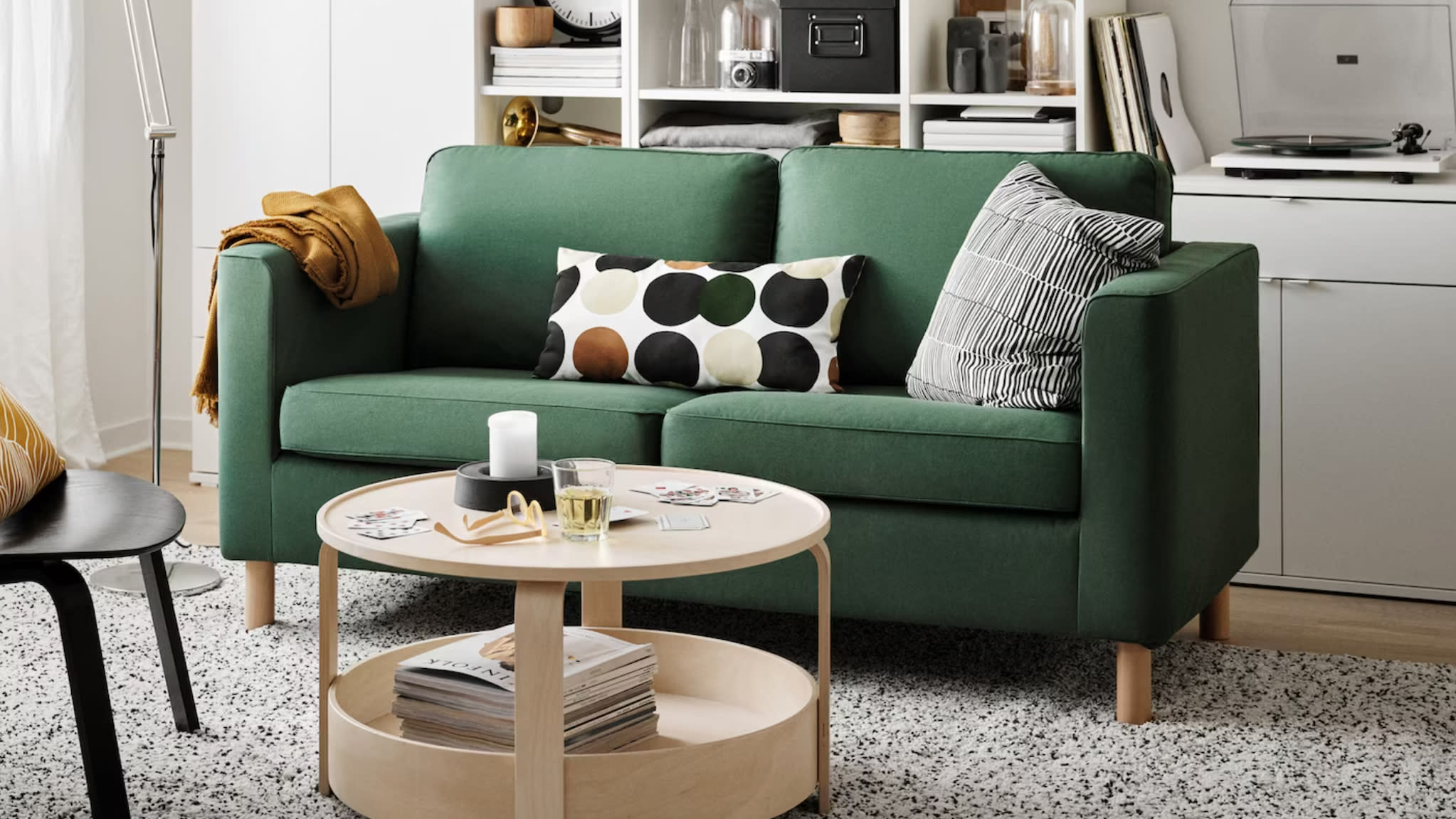 Salon avec canapé vert foncé, coussin imprimé de pastilles, table d'appoint ronde en bois et bibliothèque murale blanche