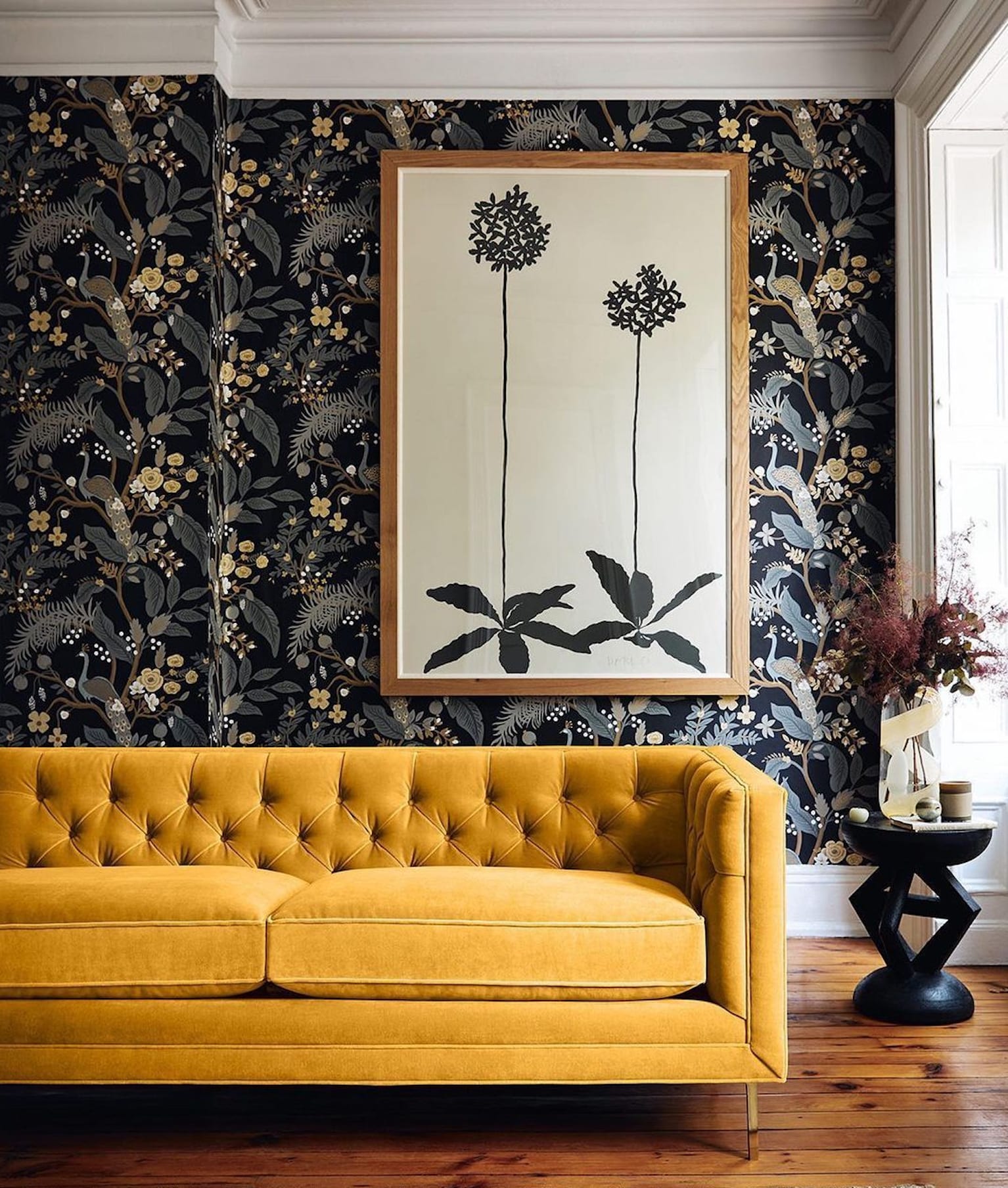 Salon avec canapé en velours capitonné jaune, papier peint imprimé floral sur fond noir