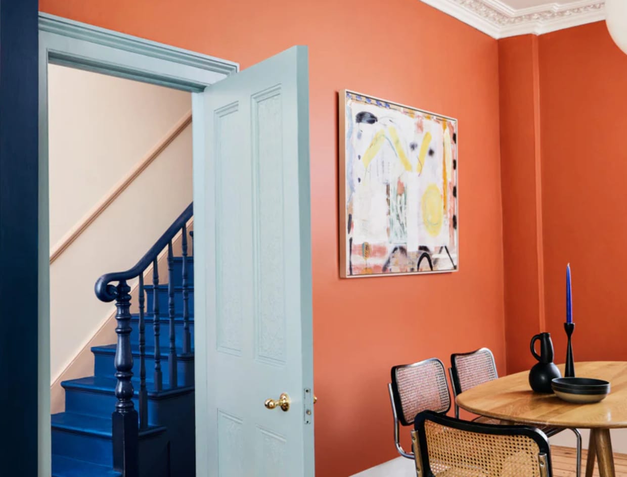 Salle à manger murs orange, table bois et chaises de type bistro, escalier bleu