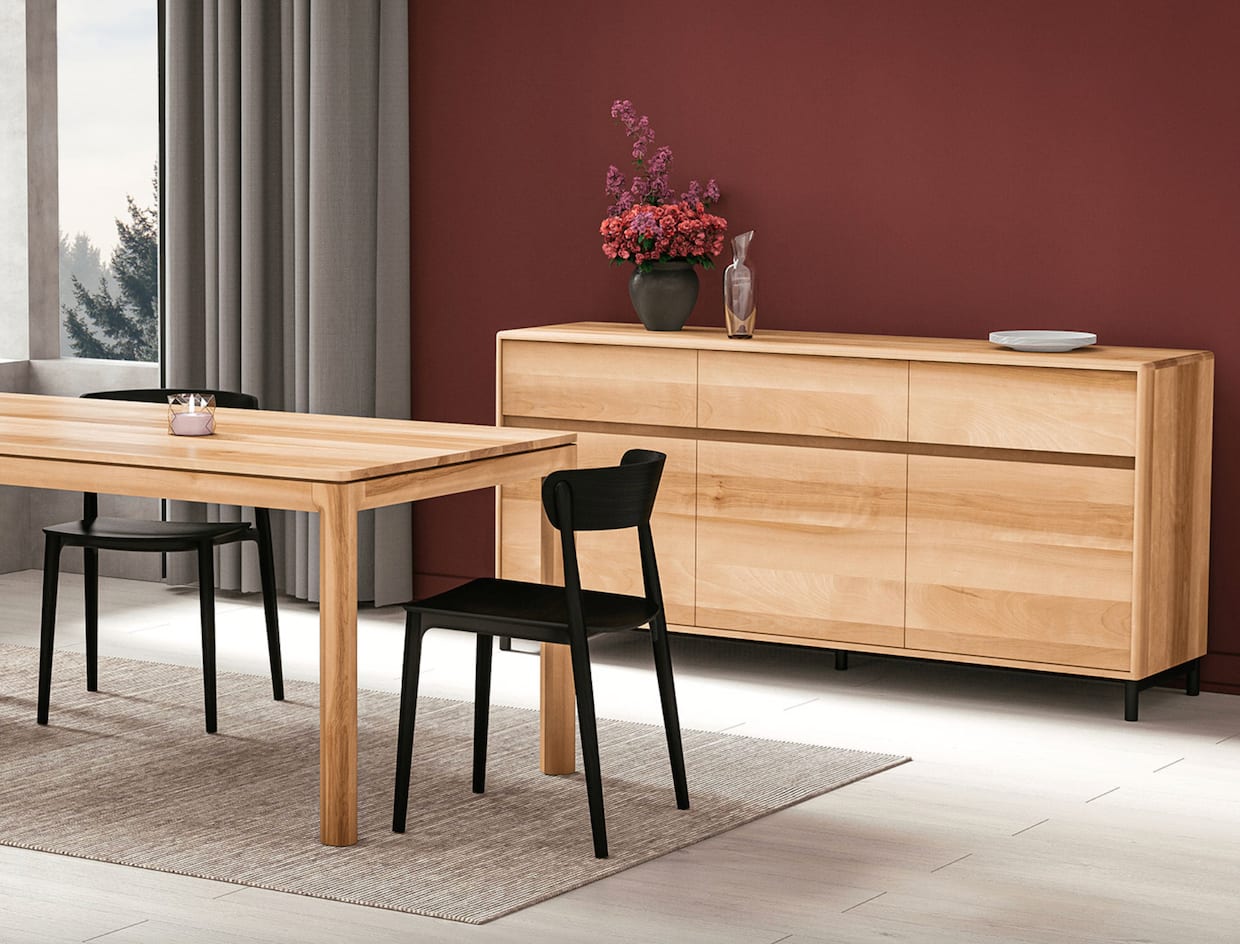 Salle à manger, table et bahut en bois blond, deux chaises noires, mur rouge rubis