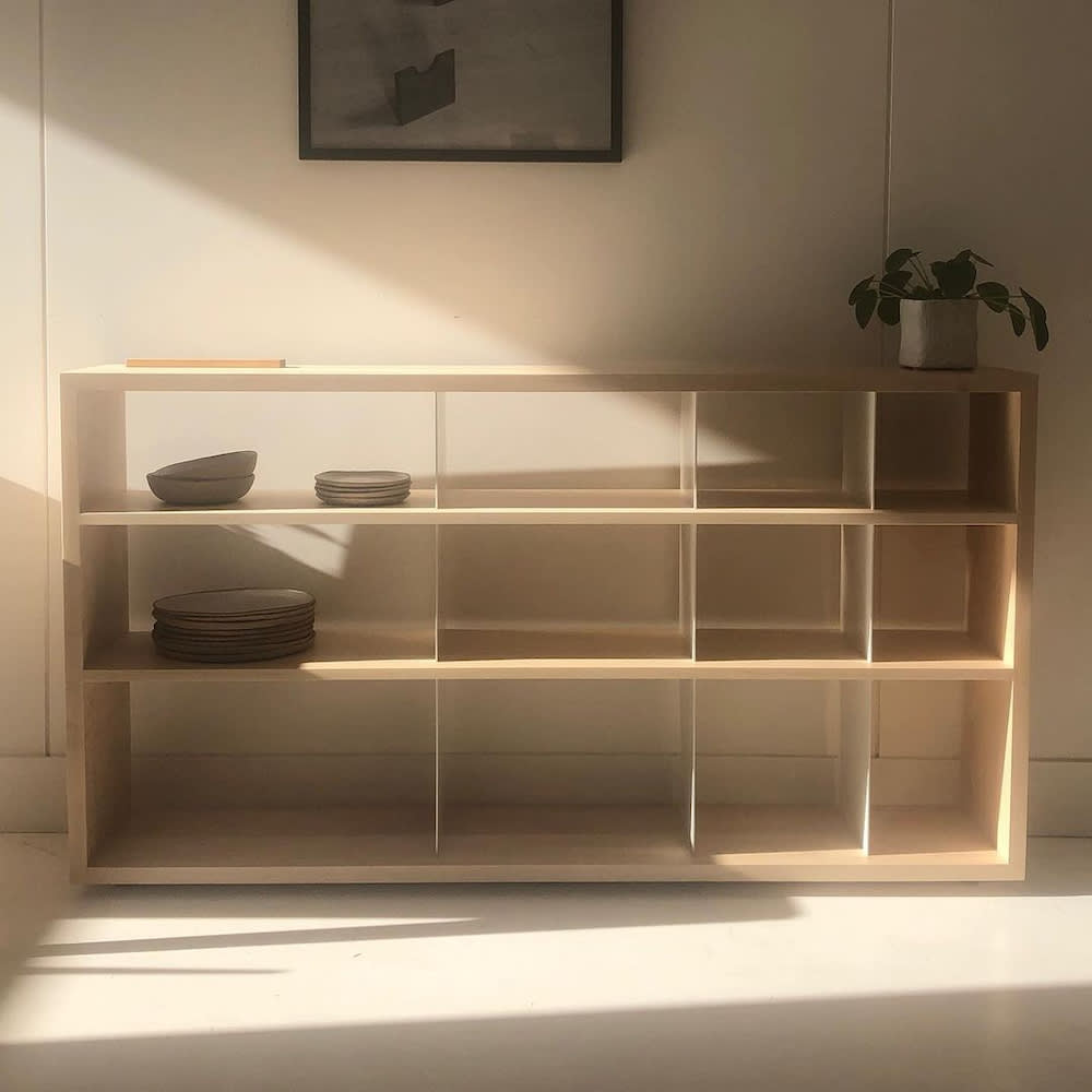 Bibliothèque basse compartimentée en bois pâle, sans fond, vaisselle et plante verte