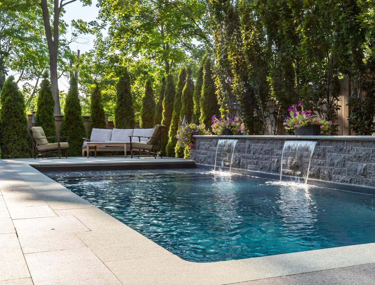 Piscine rectangulaire avec muret de pierres, trois chutes, patio et chaises coussins blanc crème