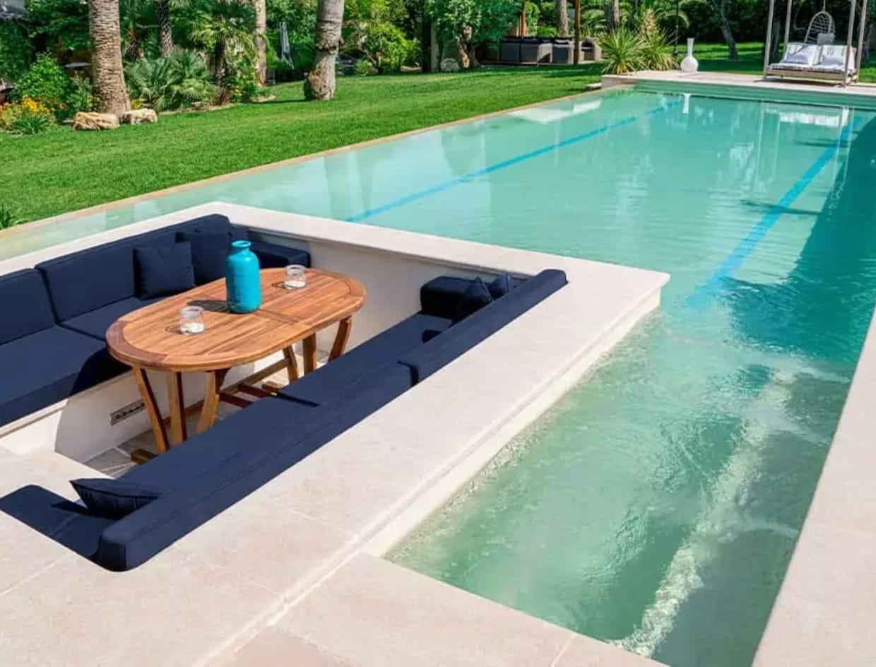 Belles piscines terrasse sur l'eau, de style ponton, avec banquettes, table en bois et coussins bleu marine
