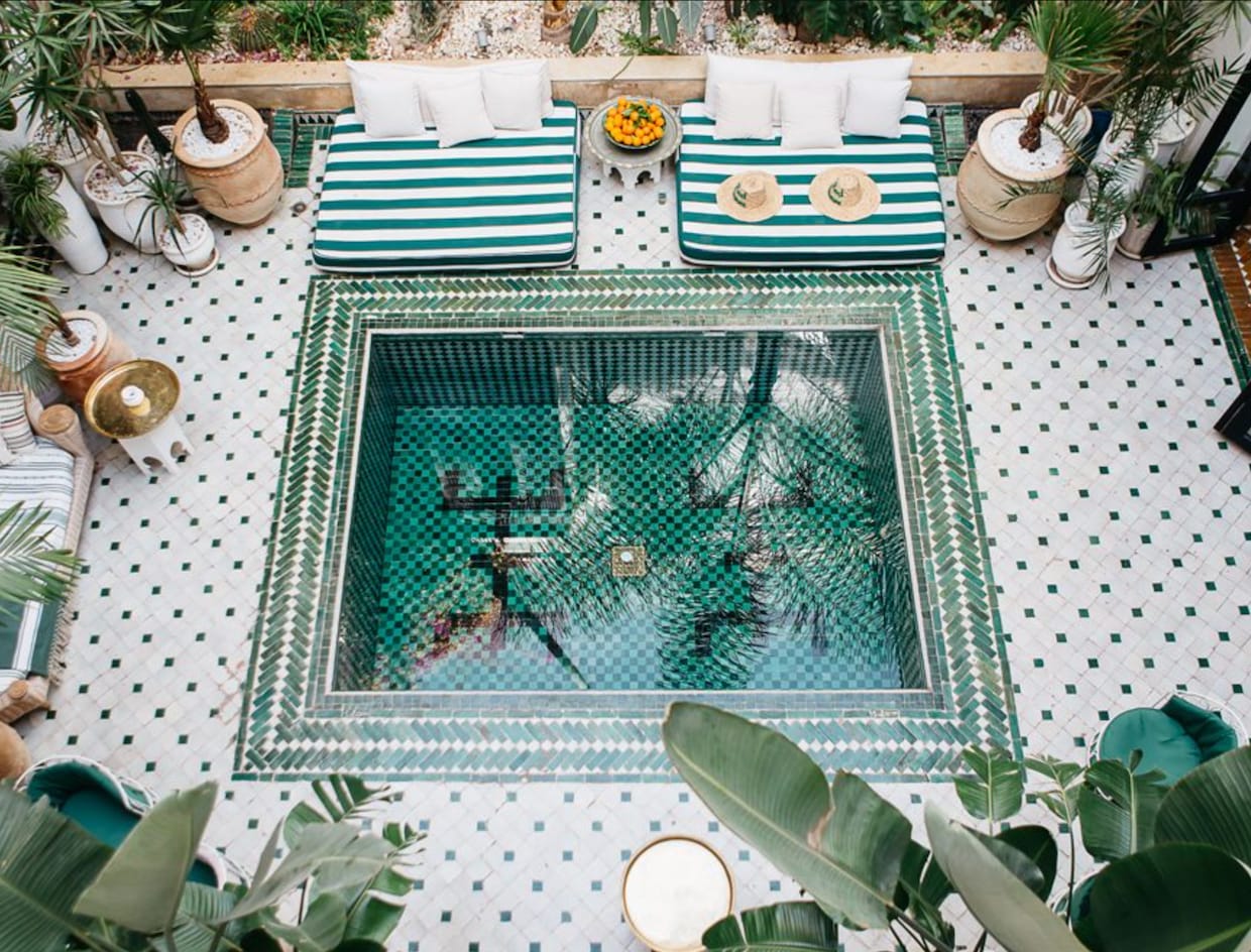 Belles piscines carrée dans la cour intérieure d'un riad, tuiles en céramique multicolore, canapés, coussins et plantes tropicales