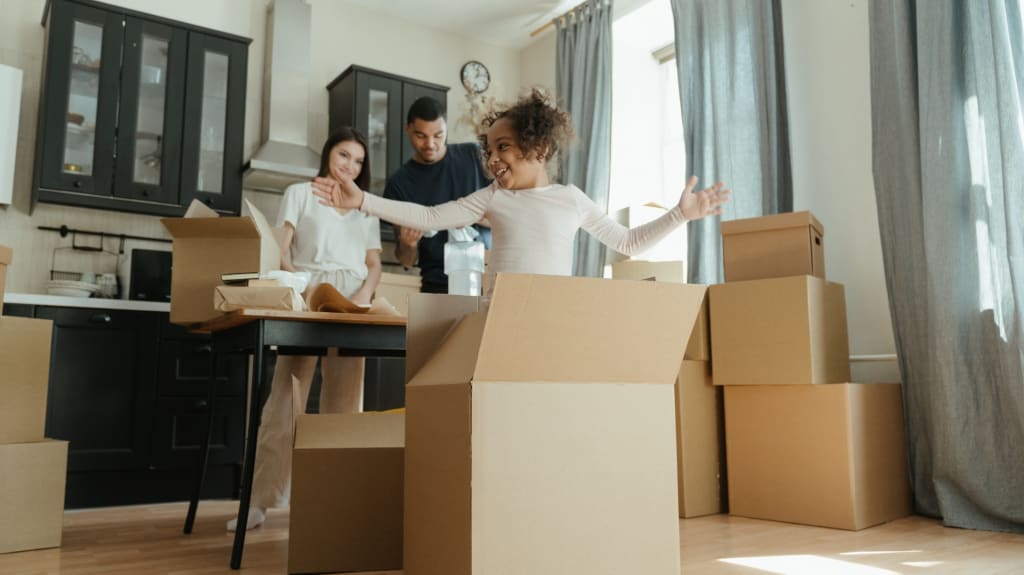 A child playing inside a box with her parents watching