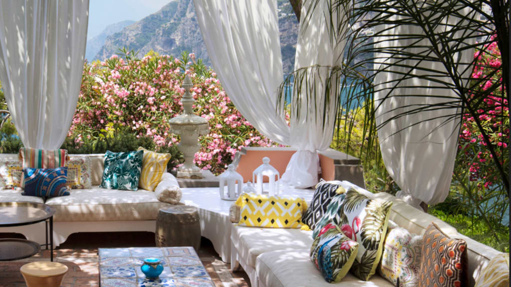 Holiday vibe home decor, flowery terrace with sofas covered in multicolored printed cushions, mountains in the background