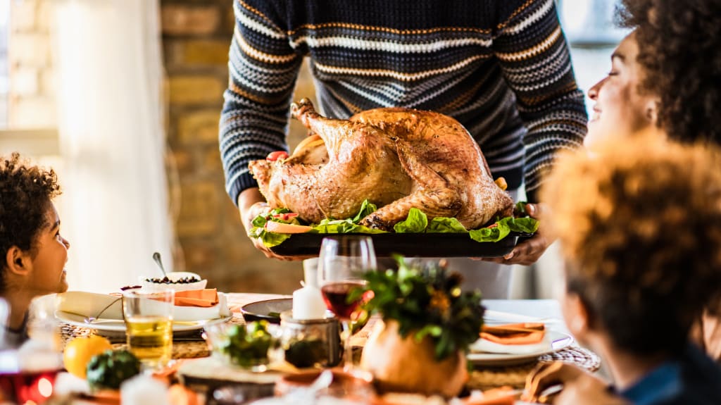 Père de famille servant une dinde grillée sur une table entourée de convives à l’occasion de l’Action de grâce
