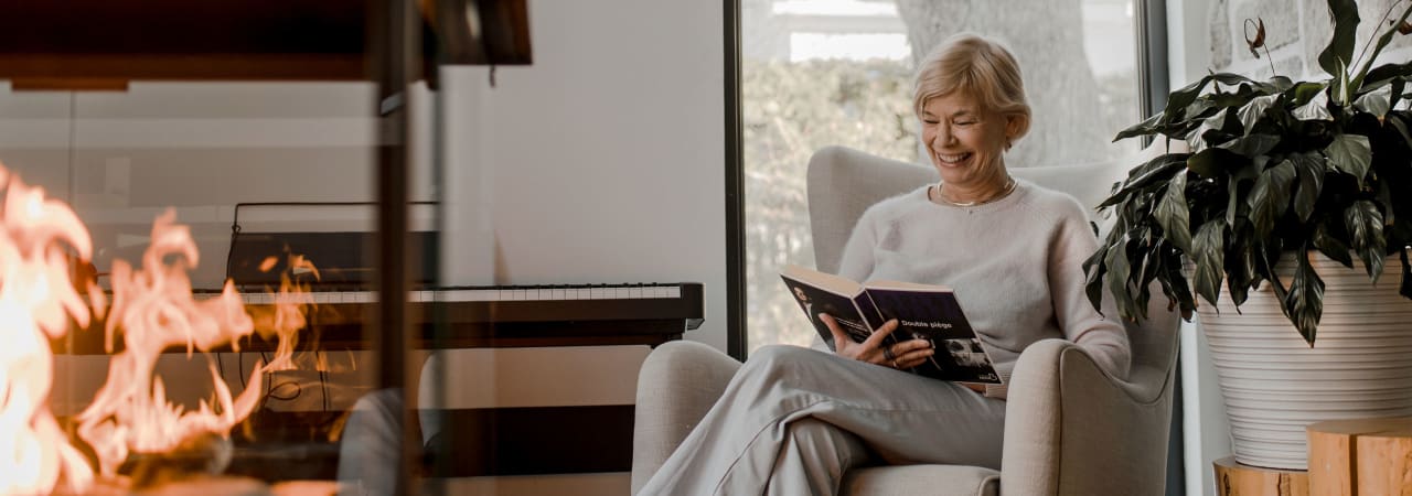 A woman sitting down in her living room reading a book by the fire