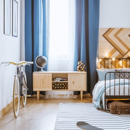 Chambre à coucher moderne pour un garçon avec de longs rideaux, un lit, un skateboard, un vélo, une armoire, des posters et une lampe