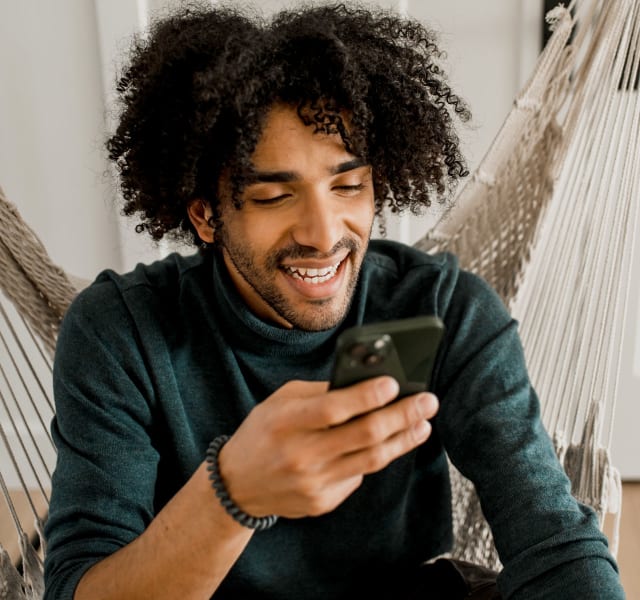 A man sitting down in a hanging rope chair and looking at his cell phone