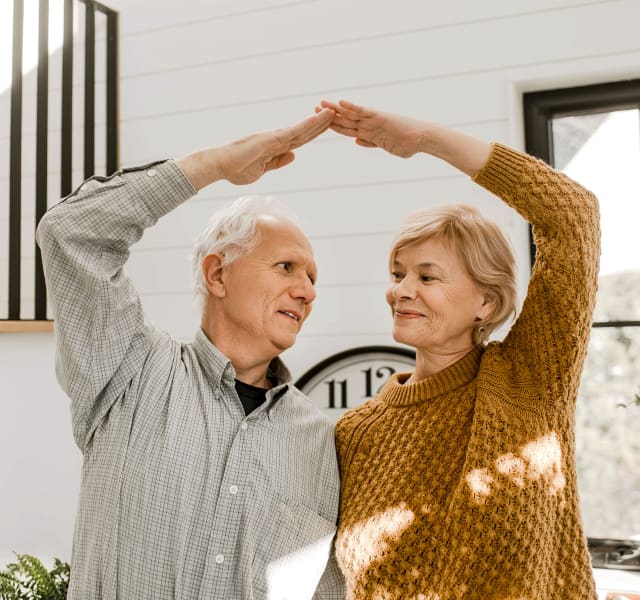 Couple of older people holding each other by the waist and forming a triangle above their head with their arms