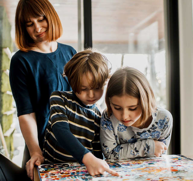 Deux enfants qui regardent un livre assis à la table de la cuisine. Leur mère est debout derrière eux.
