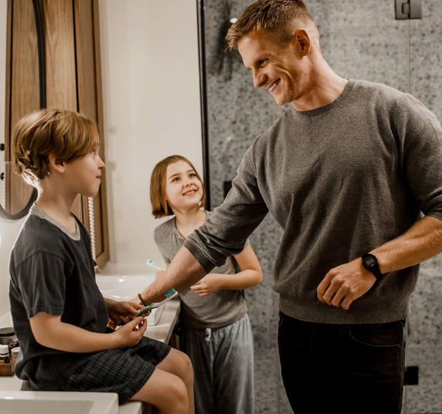 Two children brushing their teeth in the bathroom and laughing with their father