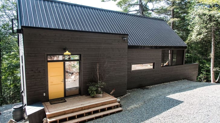 Maison noire écoresponsable avec une porte jaune en forêt