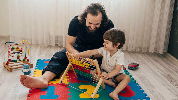 Père qui joue avec son fils et un abaque sur des carreaux de tapis matelassés