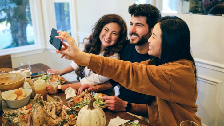 Trois amis prennent un autoportrait à leur table de Friendsgiving à l’occasion de l’Action de grâce