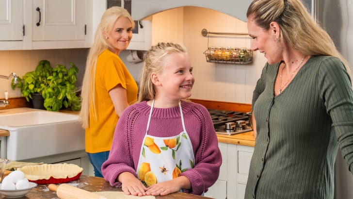 Family members in a kitchen, baking a pie and smiling at each other, by EspaceProprio