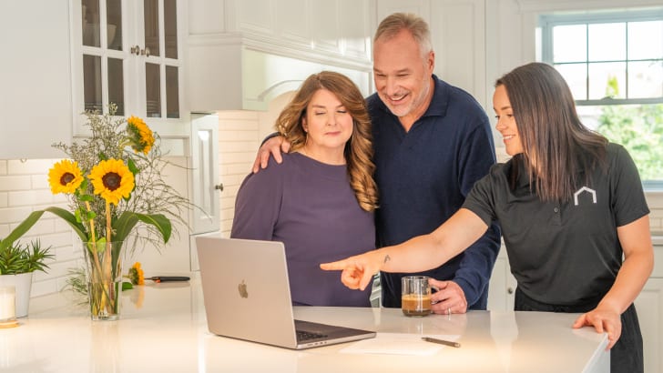 Couple in their kitchen and in front of their computer, accompanied by a person from the EspaceProprio team