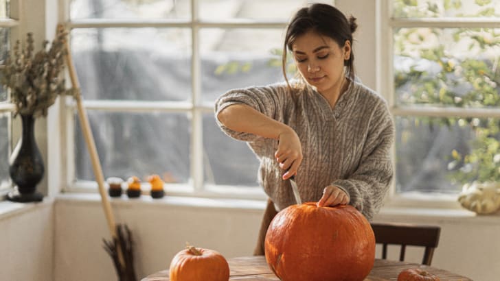 Woman in grey sweater carving a pumpkin
