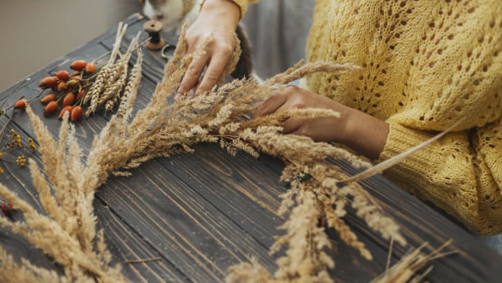 Woman making a rustic wreath on a wooden table with dried grass