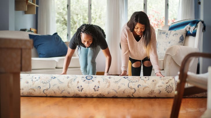 Deux femmes déroulant un tapis sur un plancher de bois d’un salon