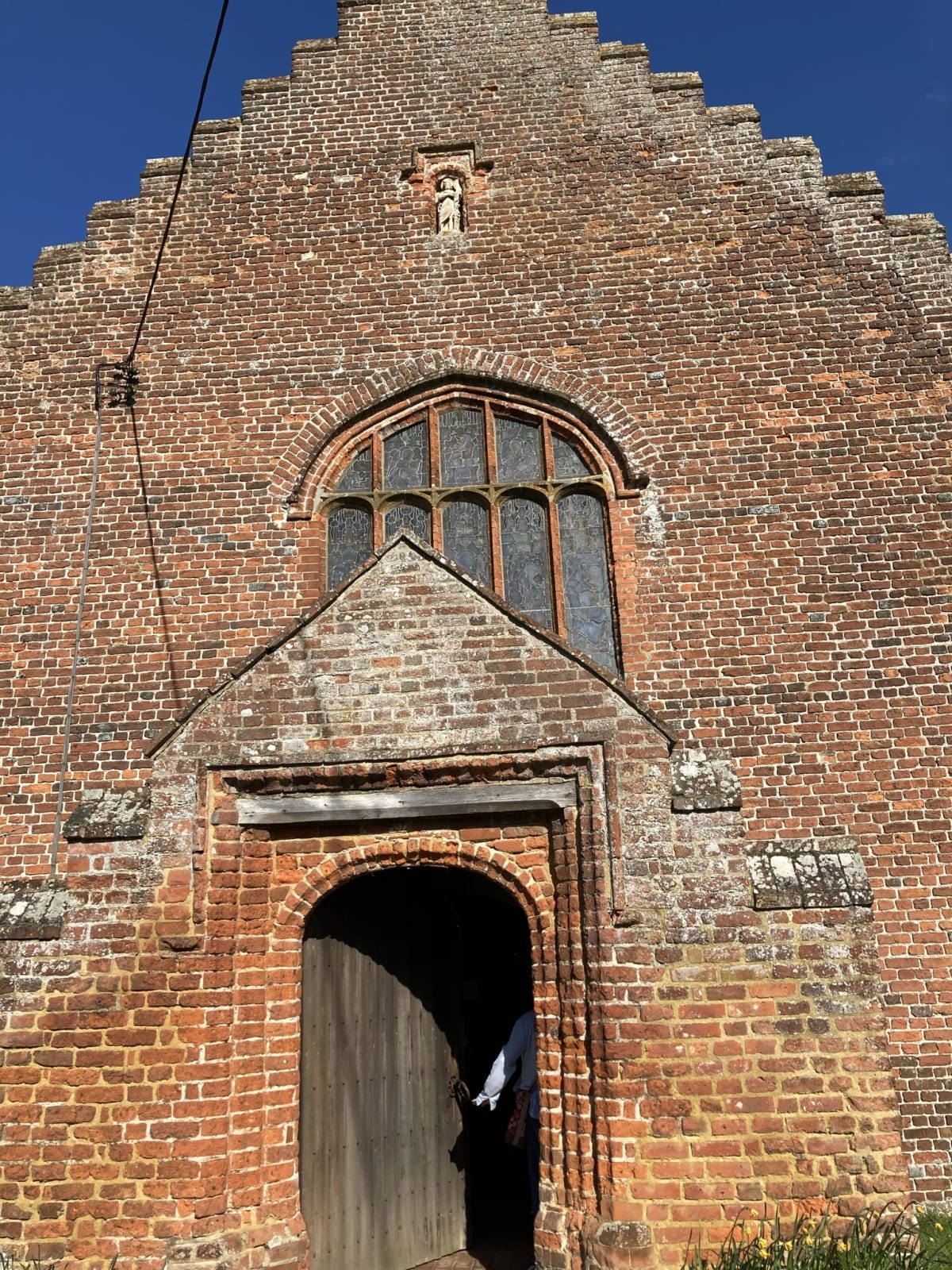 The view of the church from the west, showing the entrance and porch, as well as the figure of St John the Baptist set into a niche above the west window