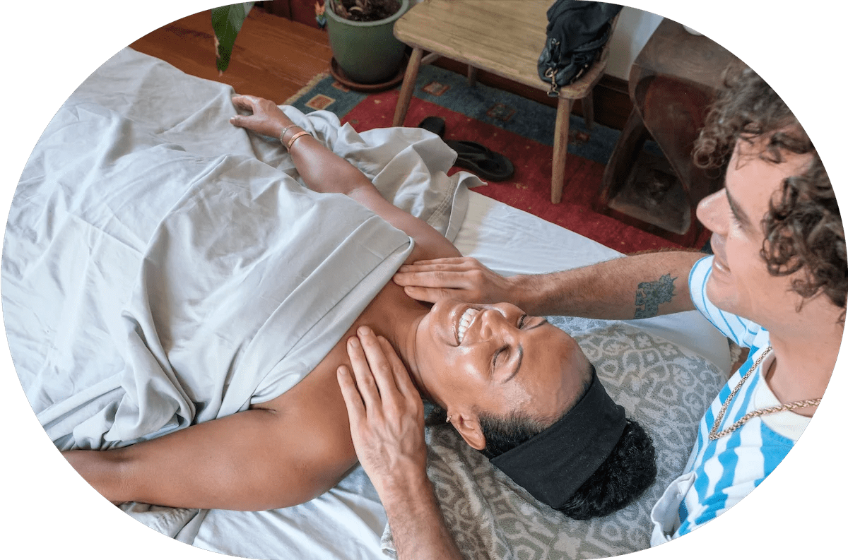 A smiling individual lying on her back having her shoulders massaged