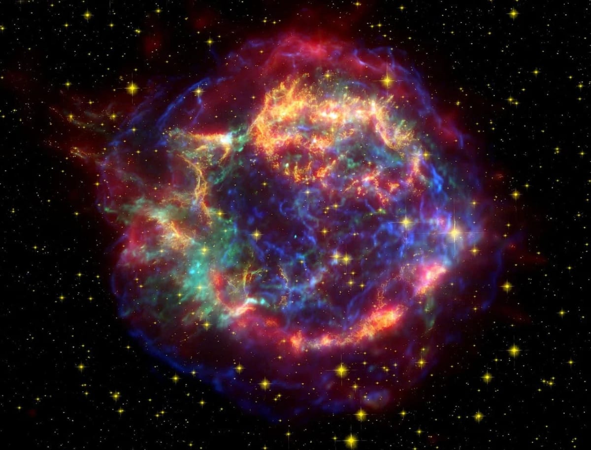 Restos de una supernova, con gases de colores vibrantes en expansión y estrellas circundantes en el fondo cósmico