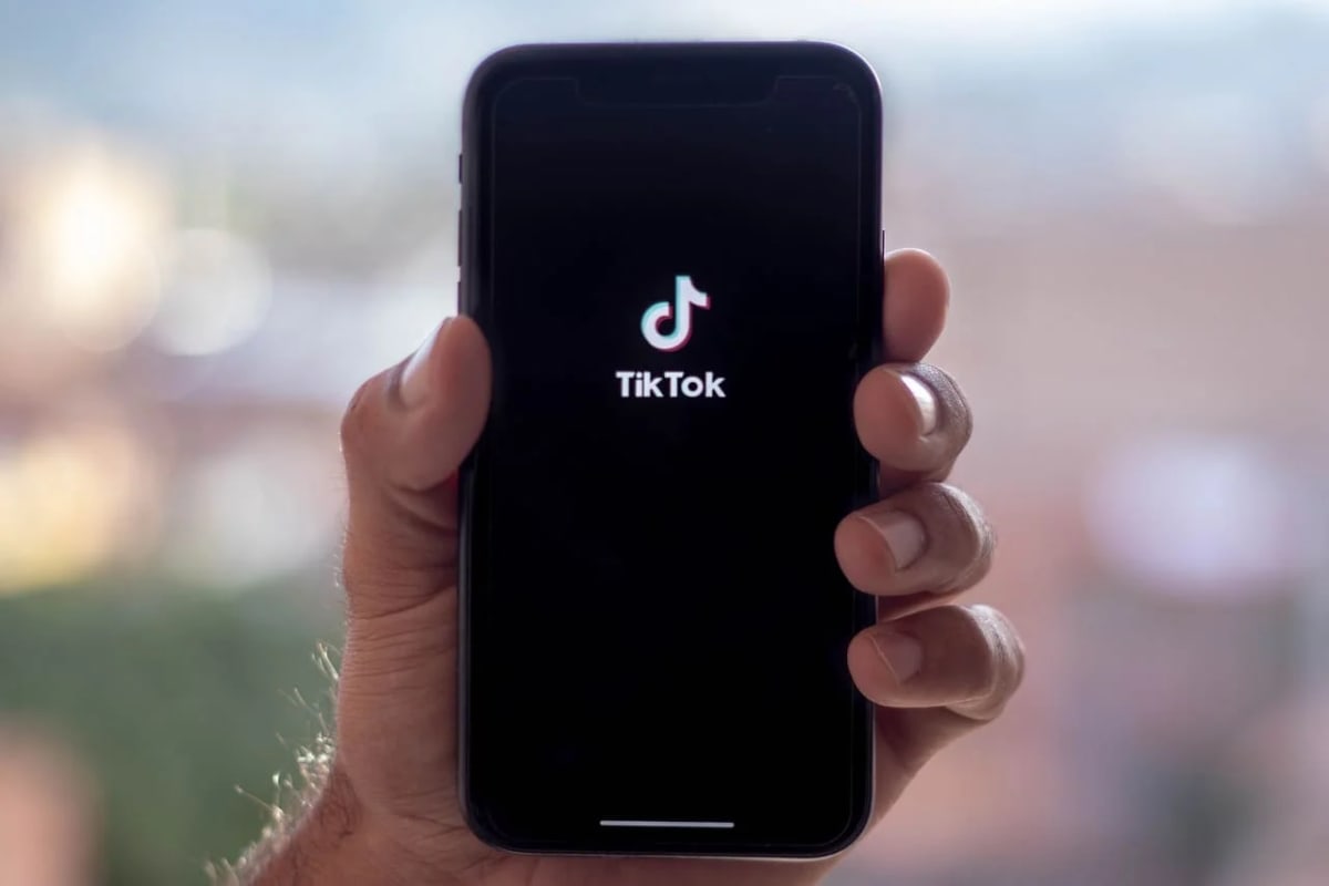 Primer plano de una mano sosteniendo un teléfono móvil con la pantalla encendida, mostrando el logotipo de TikTok.