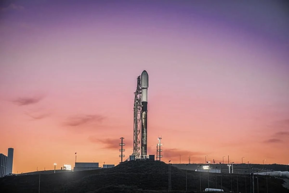 El cohete Falcon 9 de SpaceX en la plataforma de lanzamiento al amanecer, con un cielo en tonos púrpura y naranja.