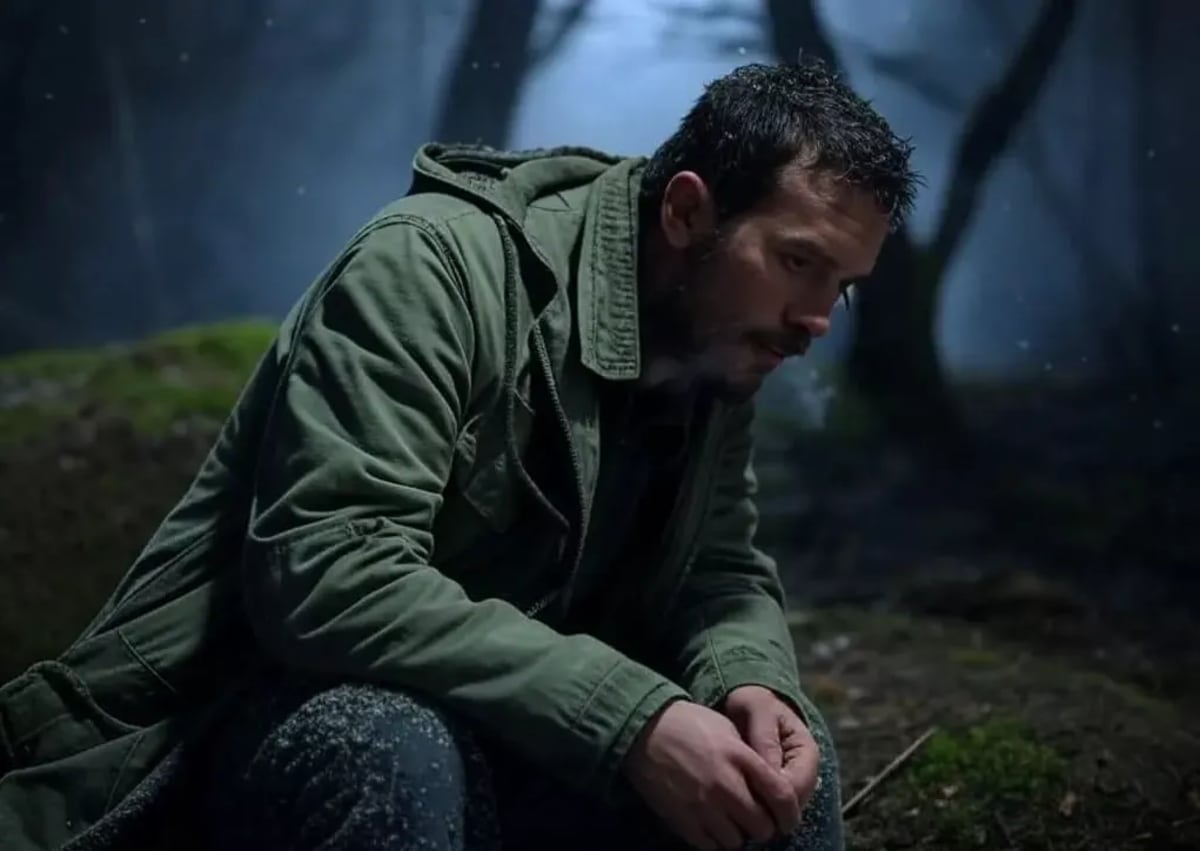 Hombre sentado en el bosque con frío, frotándose las manos mientras la nieve cae a su alrededor.