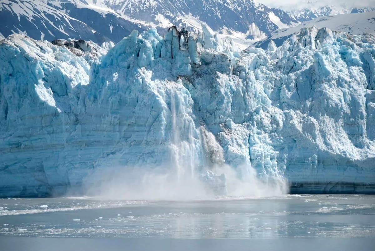 Un glaciar derritiéndose en un paisaje montañoso, con grandes fragmentos de hielo cayendo al agua en un proceso de deshielo visible.