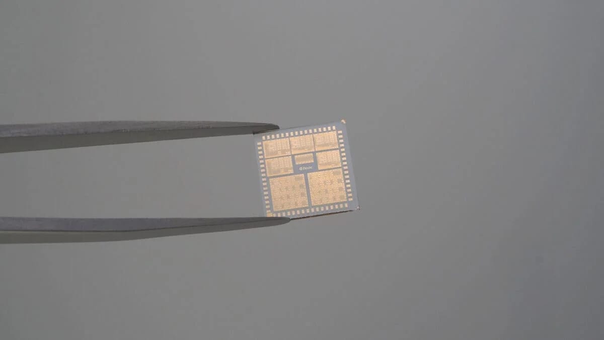 Chip semiconductor sostenido por unas pinzas de precisión sobre un fondo gris.