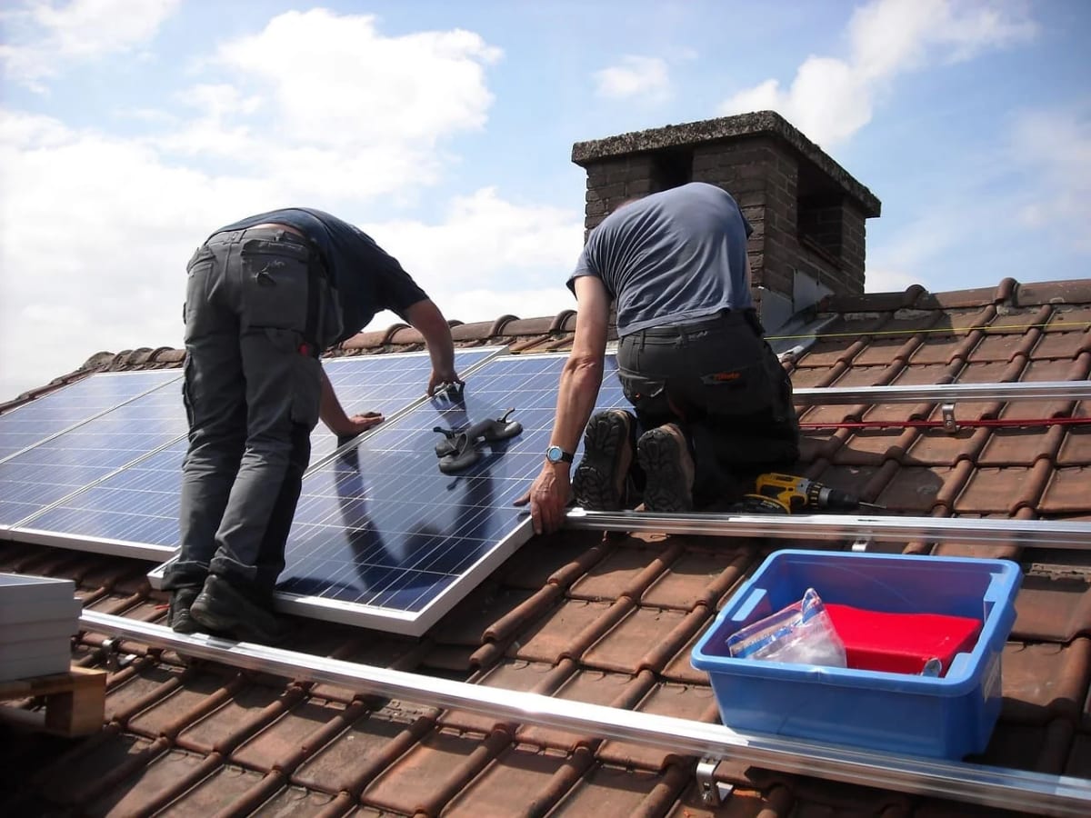Dos personas instalando paneles solares en un techo de tejas, mostrando el proceso de montaje y herramientas necesarias.