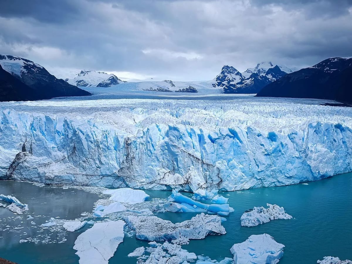 Vista panorámica del glaciar Perito Moreno en El Calafate, Argentina, con hielo flotante en el agua y montañas cubiertas de nieve al fondo.