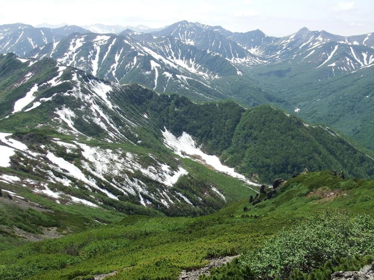 Vista panorámica de una cordillera montañosa con nieve y vegetación en primavera