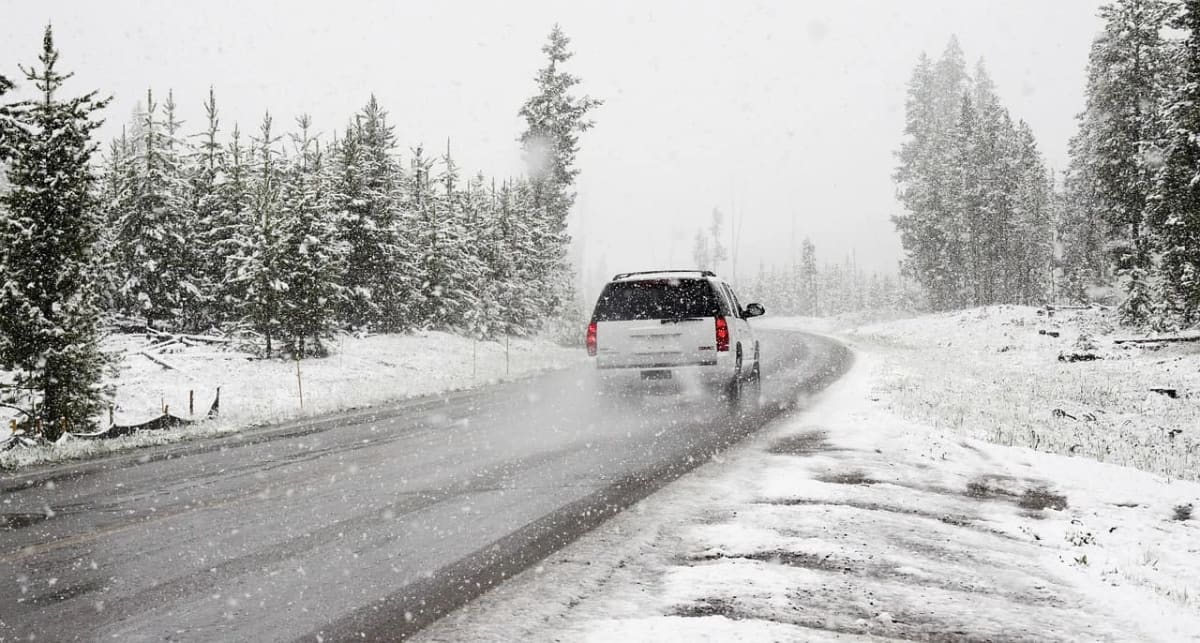 Vehículo circulando por una carretera nevada durante condiciones invernales, rodeado de árboles cubiertos de nieve.