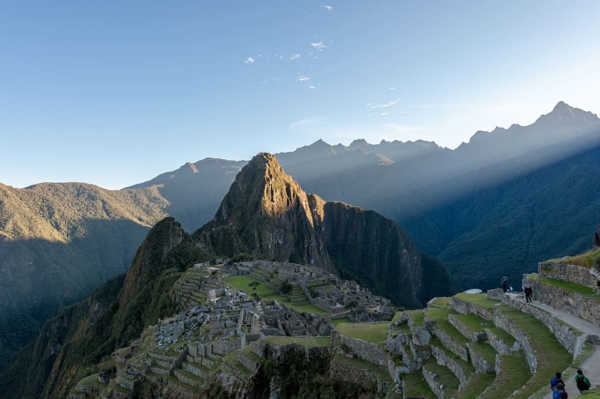 Vista panorámica de Machu Picchu al amanecer, iluminado por la luz solar y rodeado por montañas de la cordillera de los Andes.