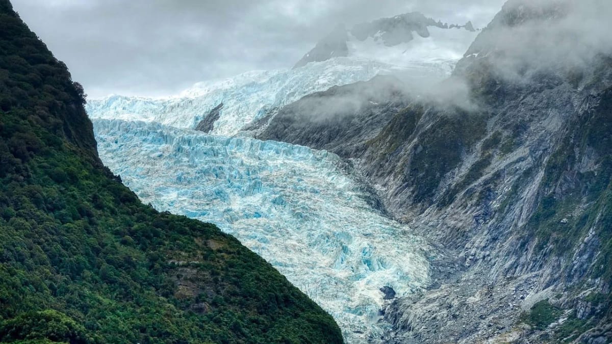 Glaciar Franz Josef descendiendo entre montañas cubiertas de vegetación y niebla.