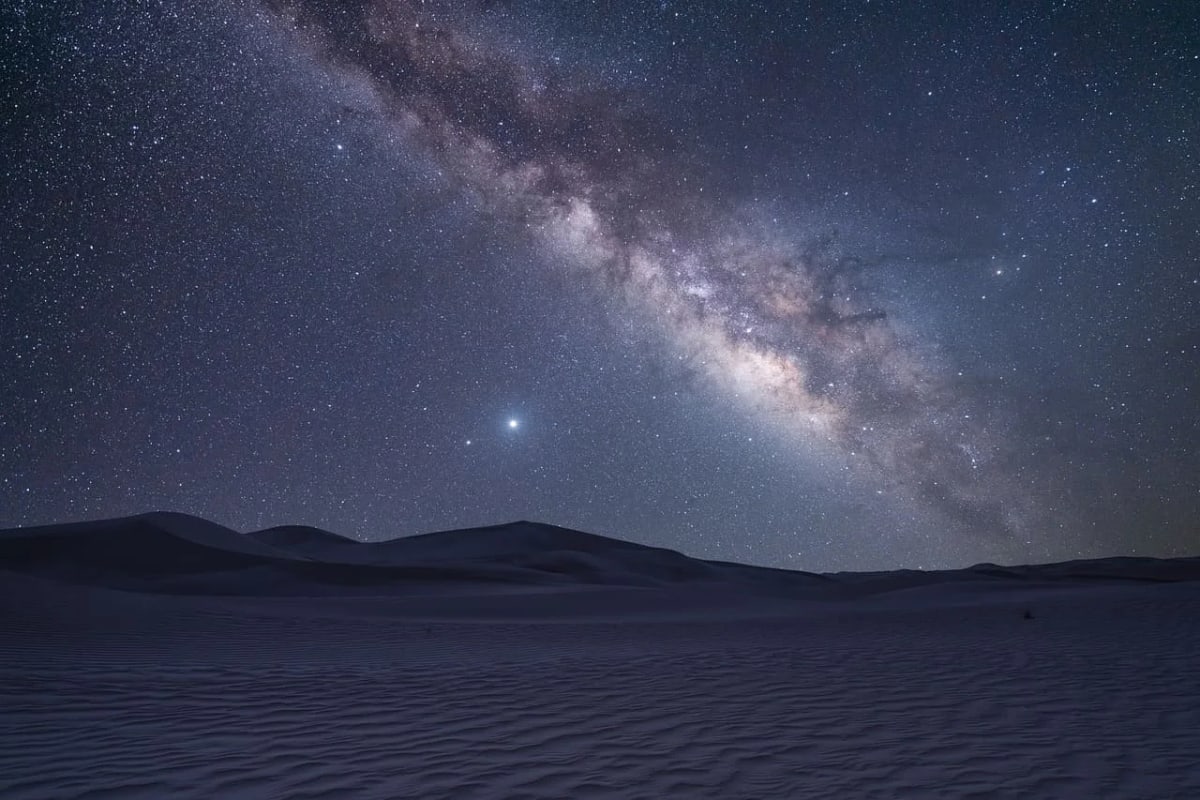 Vía Láctea iluminando el cielo estrellado sobre las dunas del desierto.