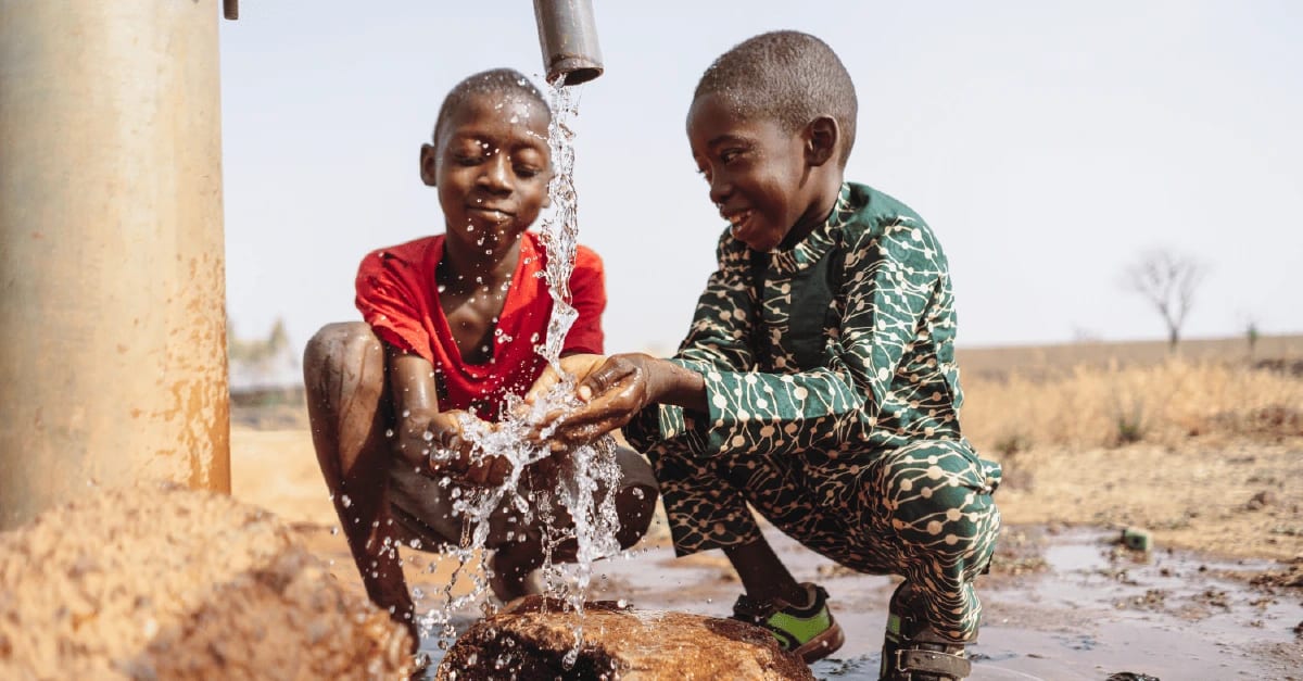 Niños junto a una fuente de agua potable limpia, símbolo del acceso seguro al agua en zonas rurales.