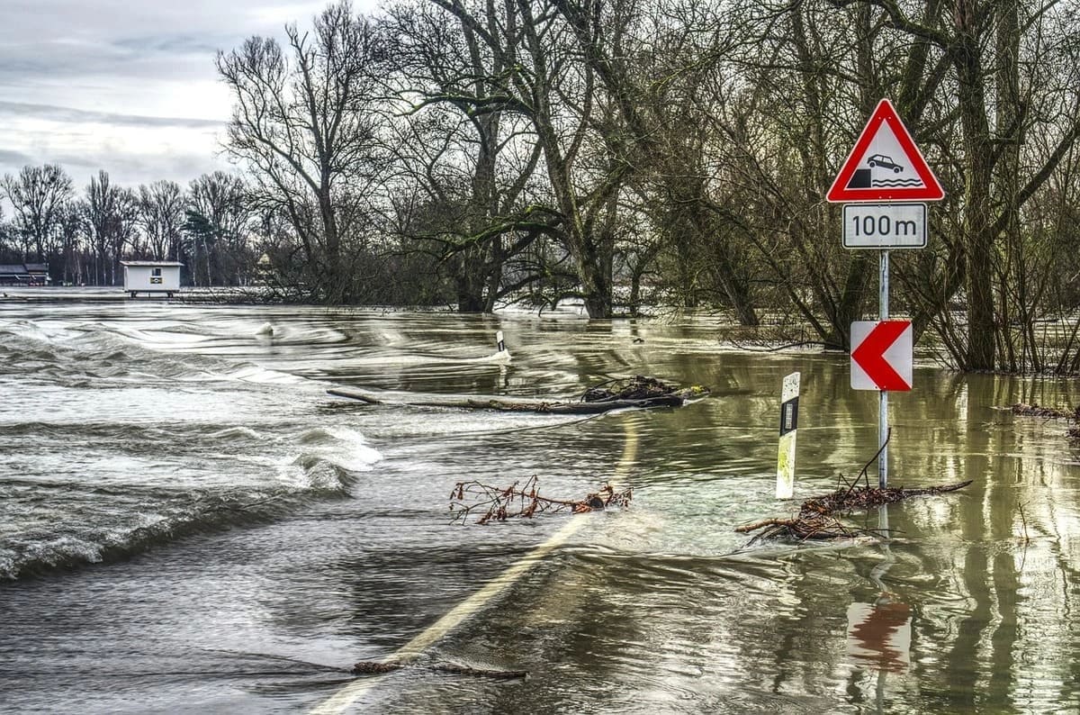 Carretera inundada con olas y señal de advertencia