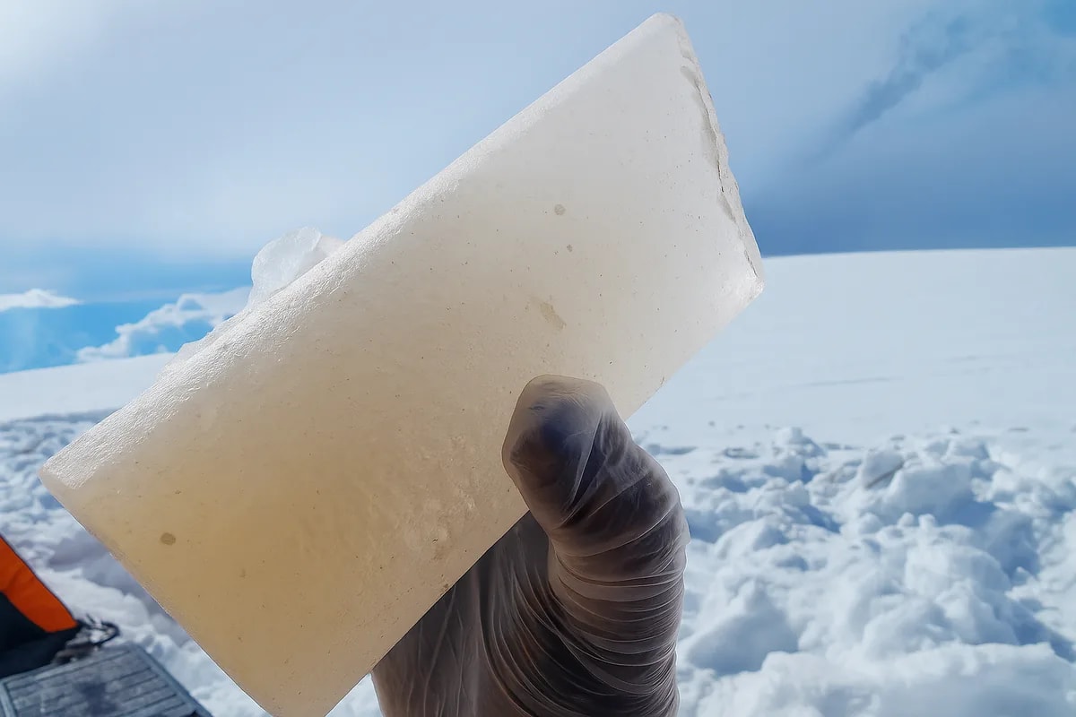 Fragmento de hielo sostenido por una mano enguantada, con fondo nevado y sin pala visible